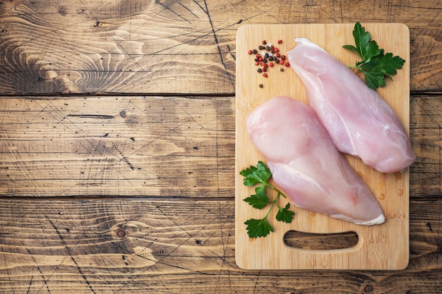 Filet de poitrine de poulet cru sur une planche à découper en bois. Fond rustique en bois. vue de dessus, espace de copie