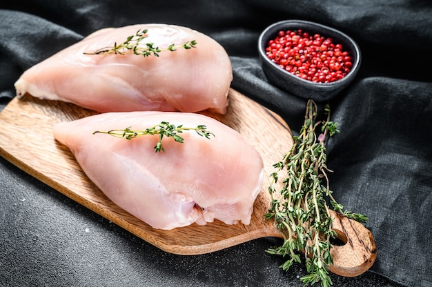 Filet de poitrine de poulet cru sur une planche à découper avec des herbes et des épices. Fond noir. Vue de dessus