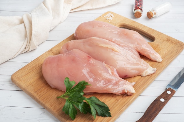 Filet de poitrine de poulet cru, viande de poulet crue sur une planche à découper. Tableau blanc, espace copie.