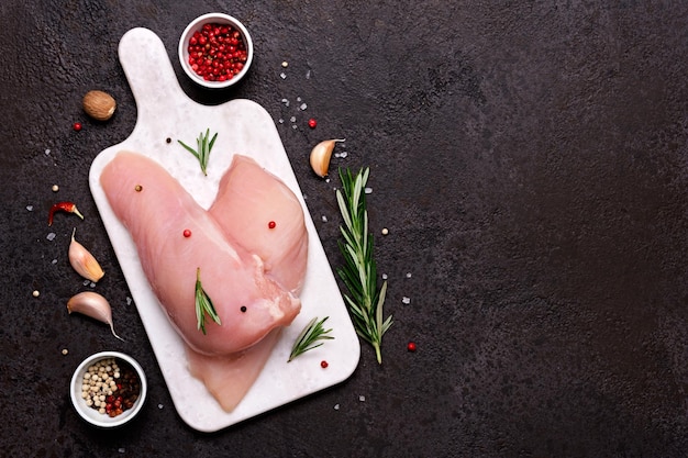 Filet de poitrine de poulet frais sur une planche à découper avec des épices et des herbes sur fond de pierre noire Préparation pour la cuisson