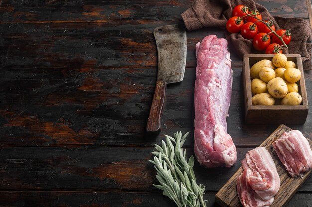 Filet de porc biologique avec ingrédients et herbes pour griller ou cuire au four, sauge, pomme de terre sertie d'un vieux couteau de couperet de boucher, sur un vieux fond de table en bois foncé, avec fond et espace pour le texte