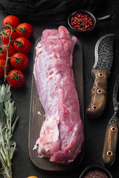 Filet de porc cru à la sauge, sur planche à découper en bois, avec couteau barbecue et fourchette à viande, sur pierre noire