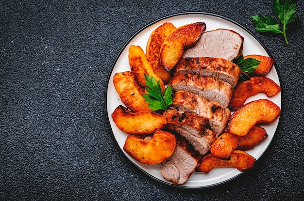 Filet de porc frit avec des tranches de coing ou de pomme servi sur une assiette vue de dessus de fond de tableau noir