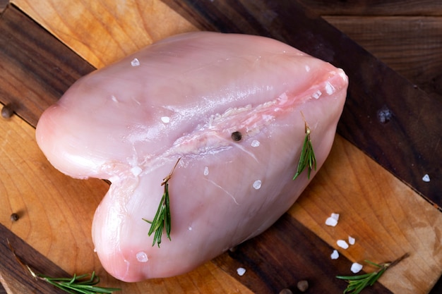 Filet de poulet cru à l'ail, poivre et romarin sur une surface en bois