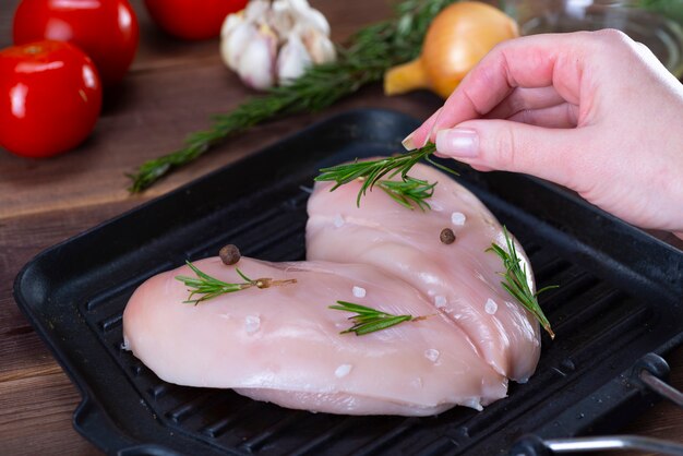 Filet de poulet cru à l'ail, poivre et romarin sur une surface en bois