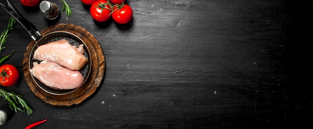 Filet de poulet cru aux tomates et herbes. sur le tableau noir.