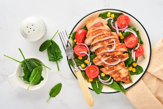 Filet de poulet avec salade d'épinards, tomates cerises, bleuet et oignon. La nourriture saine. Régime céto, concept de déjeuner diététique. Vue de dessus sur une surface blanche.