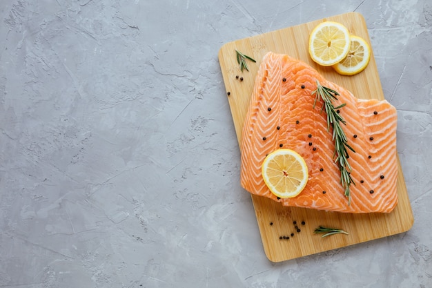 Filet de saumon cru au citron romarin et poivre sur planche à découper poisson atlantique sauvage biologique frais sur fond de pierre grise vue de dessus cuisine méditerranéenne concept d'alimentation saine et diététique