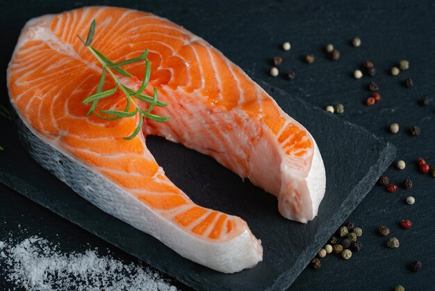 Filet de saumon cru et ingrédients pour la cuisson des assaisonnements et des herbes sur fond sombre