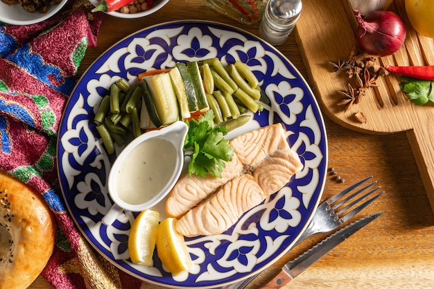 Filet de saumon cuit à la vapeur avec carottes, courgettes et jeunes haricots verts sur une assiette avec des ornements traditionnels ouzbeks