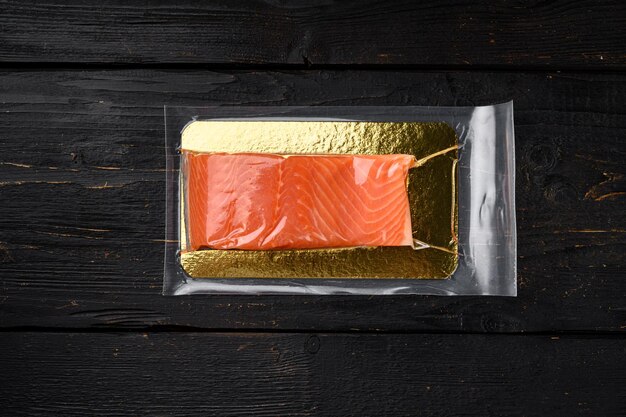 Filet de saumon emballage sous vide viande de poisson sur fond de table en bois noir vue de dessus mise à plat avec espace de copie pour le texte