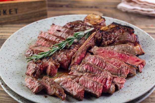 Filet de steak barbecue de viande de porc de boeuf rouge grillé avec brin de romarin et sauce piquante servi sur plaque blanche.