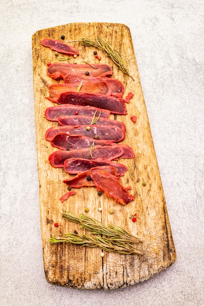 Filet de viande de boeuf séchée avec du romarin sec et du mélange de poivre sur planche de bois vintage