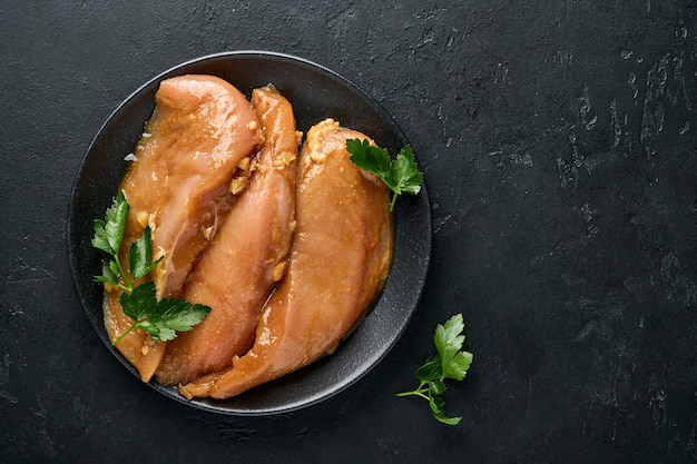 Photo filet de viande de poulet cru mariné dans une sauce soja teriyaki, oignons, ail et poivre en plaque noire