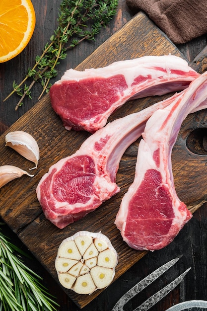 Filets D'agneau Crus Sur L'os Avec Des Ingrédients Herbes Orange Carotte Sur La Vieille Table En Bois Sombre Vue De Dessus D'arrière-plan Mise à Plat