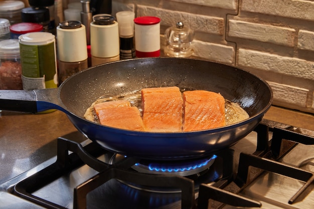 Des filets frais de poisson Salomon sont frits dans une poêle sur une cuisinière à gaz.