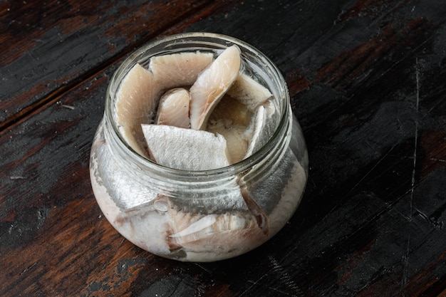 Filets de hareng sauvage en conserve, dans un bocal en verre, sur une vieille table en bois foncé