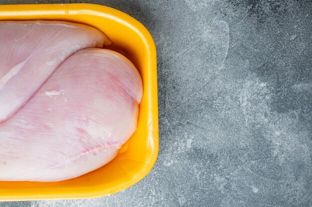 Filets de poitrine de poulet cru dans le bac, sur fond gris avec espace de copie pour le texte