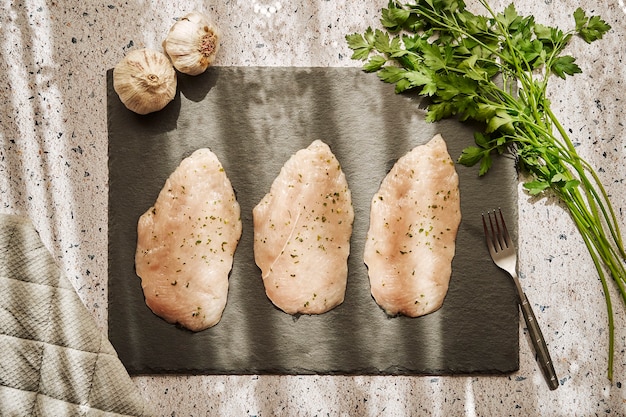 Filets de poitrine de poulet crus sur une ardoise sur une table en granit avec du persil