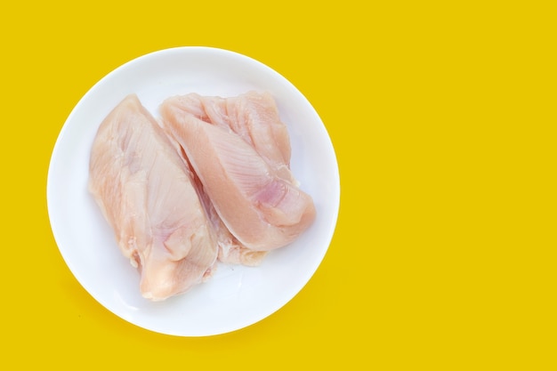 Filets de poitrine de poulet crus non cuits dans une assiette blanche sur fond jaune.