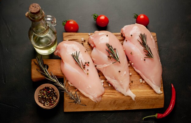 Filets de poitrine de poulet crus, prêts à cuire sur une planche à découper en bois avec des épices.