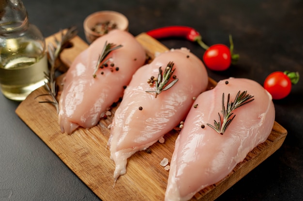 Filets de poitrine de poulet crus, prêts à cuire sur une planche à découper en bois avec des épices.