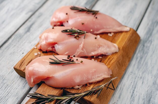 Filets de poitrine de poulet crus, prêts à cuire sur une planche à découper en bois avec des épices.