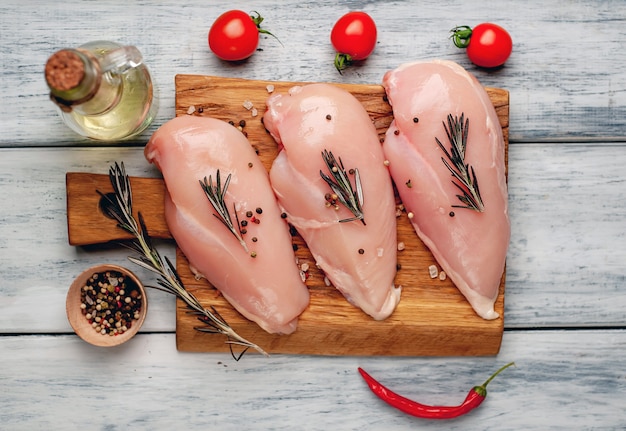 Filets de poitrine de poulet crus, prêts à cuire sur une planche à découper en bois avec des épices.