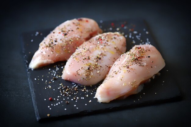 Photo filets de poulet cru aux épices sur une planche de pierre.