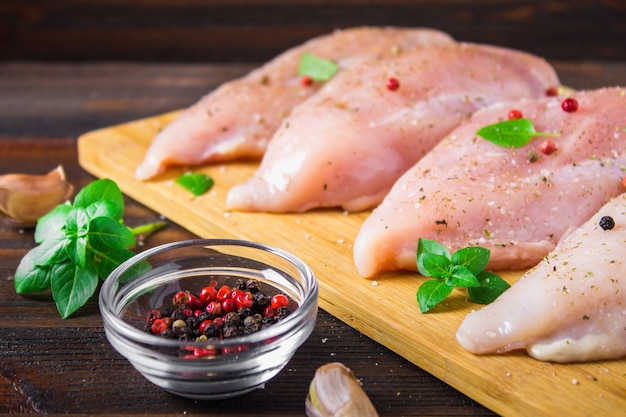 Filets de poulet cru sur une planche à découper dans le contexte d&#39;une table en bois.