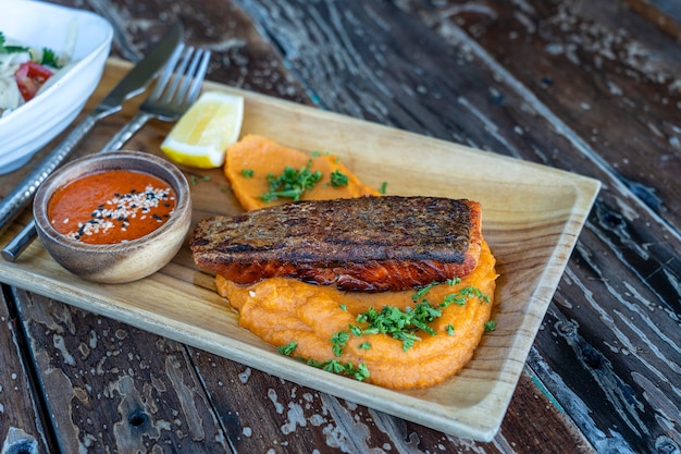 Filets de saumon frits servis avec garniture de légumes sur assiette en bois et sauce, gros plan. Filet de saumon rôti avec purée de patates douces.