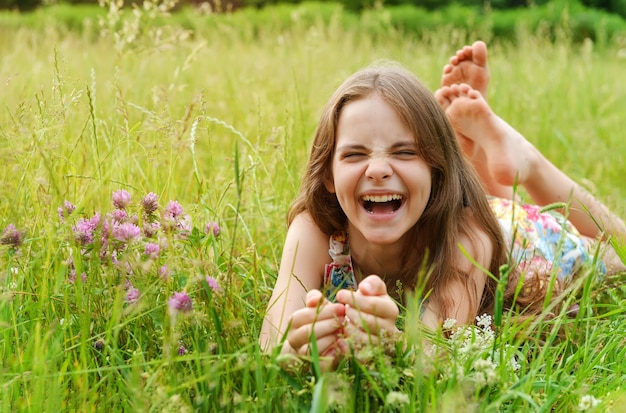 Fille de 10 ans se trouve sur l'herbe parmi les fleurs et rit