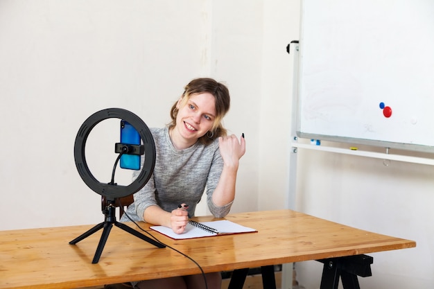 Fille de 16 ans d'enregistrement vidéo sur smartphone et s'éclairant avec une lampe annulaire à table dans une pièce lumineuse