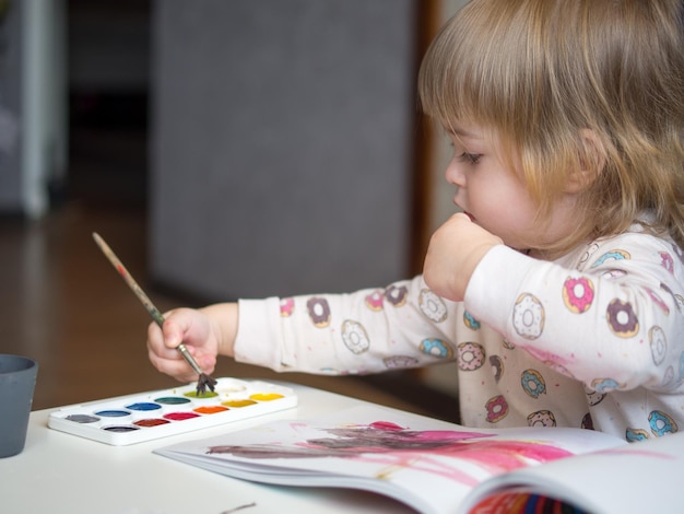 Une fille de 2 ans est assise à une table et apprend à dessiner avec des aquarelles multicolores La créativité des enfants Les loisirs des enfants