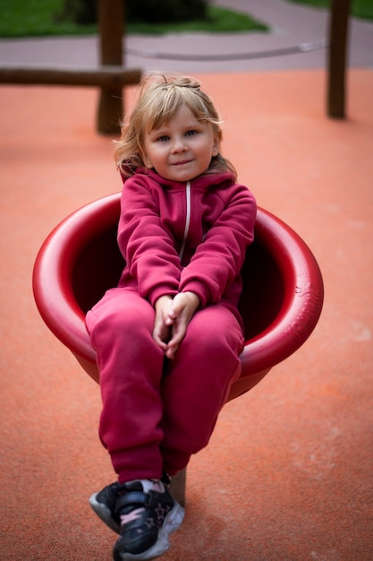 fille 5 ans blonde en vêtements rouges joue sur le terrain de jeu enfance heureuse