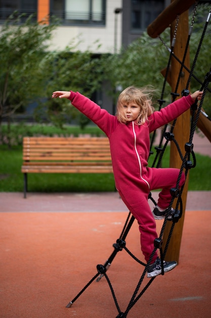 Fille 5 ans blonde en vêtements rouges joue sur le terrain de jeu