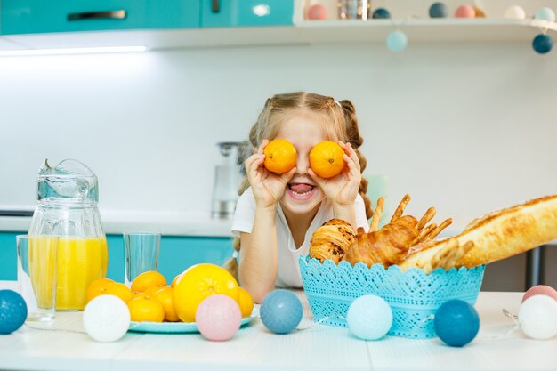 Une fille de 7-8 ans est assise dans la cuisine et fait des yeux avec une mandarine.