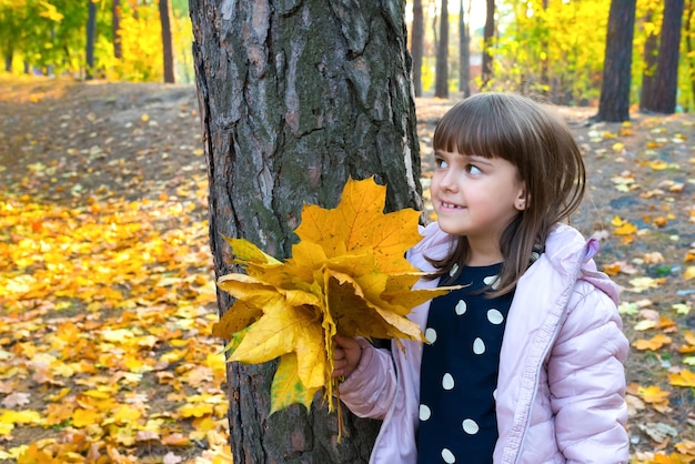 Une fille de 78 ans avec des feuilles d'automne jaunes joue dans un parc d'automne ensoleillé