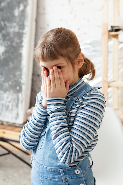 Fille de 8 ans frustrée en salopette couvrant son visage avec les mains