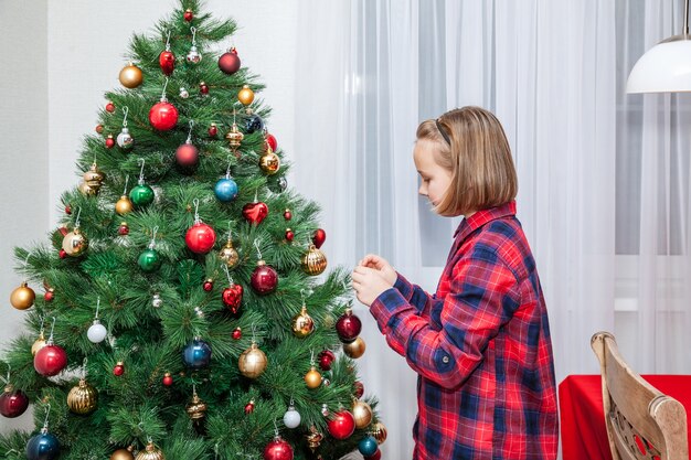 La fille accroche un jouet de Noël sur l'arbre de Noël