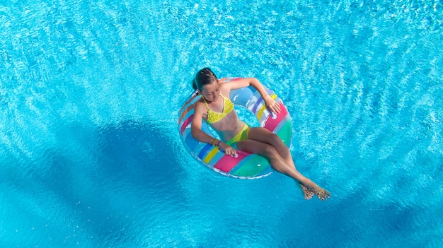 Fille active dans la piscine vue de dessus aérienne d'en haut, l'enfant nage sur l'anneau gonflable beignet, l'enfant s'amuse dans l'eau bleue sur les vacances en famille