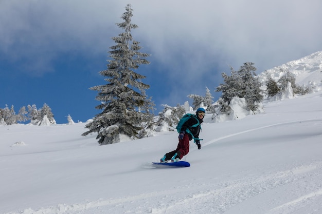 Une fille active monte sur un snowboard freeride sur une pente enneigée dans un terrain alpin de l'arrière-pays dans les montagnes blanches