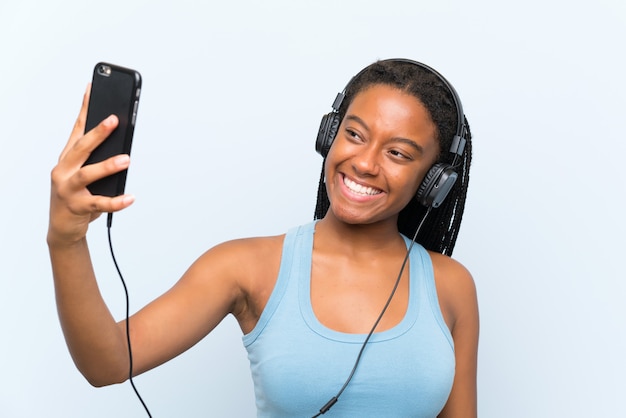 Fille adolescente afro-américaine avec de longs cheveux tressés écouter de la musique avec un téléphone portable