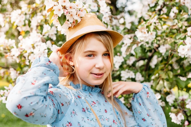 Une fille, une adolescente au chapeau se promène au printemps dans la ville, des arbres en fleurs, un pommier