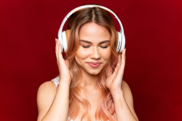 Fille adolescente aux cheveux roses sur fond rouge isolé à l'écoute de la musique