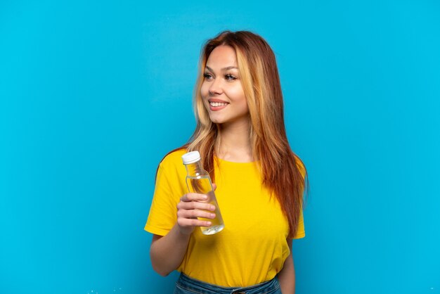 Fille adolescente avec une bouteille d'eau sur fond bleu isolé à côté