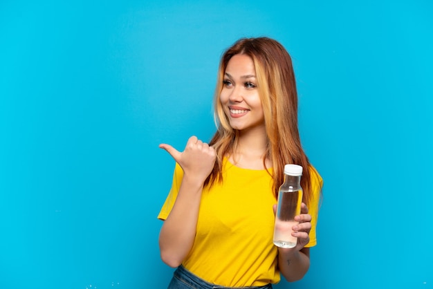 Fille adolescente avec une bouteille d'eau sur fond bleu isolé pointant vers le côté pour présenter un produit