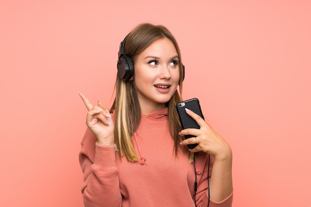 Fille adolescente écoutant de la musique avec un téléphone portable sur un mur rose isolé