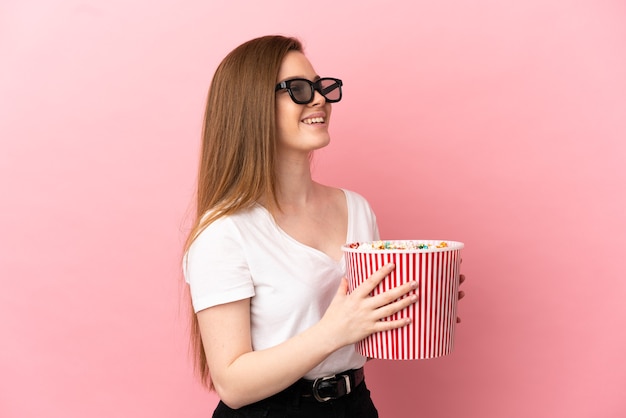 Fille adolescente sur fond rose isolé avec des lunettes 3d et tenant un grand seau de pop-corn