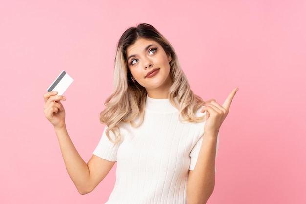 Fille adolescente sur fond rose isolé tenant une carte de crédit